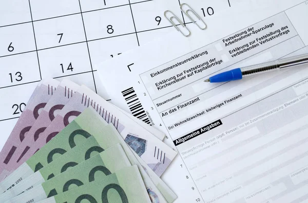 Formulario de impuestos alemán con bolígrafo y billetes de dinero europeo se encuentra en el calendario de la oficina. Contribuyentes en Alemania que utilizan la moneda del euro para pagar impuestos — Foto de Stock