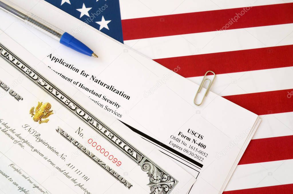 N-400 Application for Naturalization and Certificate of naturalization lies on United States flag with blue pen from Department of Homeland Security