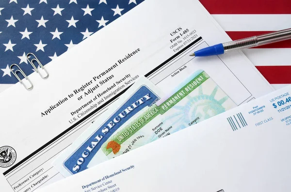 I-485 Application to register permanent residence or adjust status form and green card from dv-lottery with social security number lies on United States flag with USCIS envelope — 스톡 사진