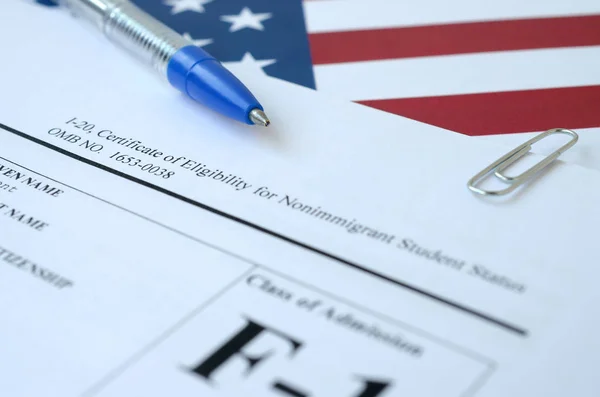 I-20 Сертифікат про право на неіммігрантський статус студента лежить на прапорі Сполучених Штатів з блакитною ручкою від Департаменту національної безпеки — стокове фото