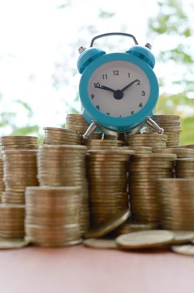 Blue alarm clock on big amount of shiny ukrainian old 1 hryvnia coin stacks close up on blurred green trees backdrop. The concept of financial planning and business time management — 스톡 사진