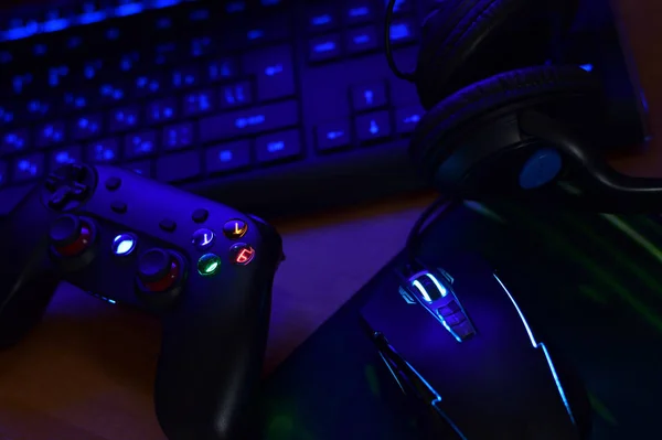 O gamepad moderno e o mouse de jogo estão com teclado e fones de ouvido na mesa na cena escura da sala de jogos. Conceito de comunidade de jogadores de videogame online — Fotografia de Stock