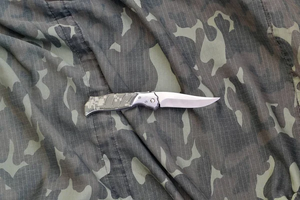 Military knife on army camouflage clothes close up. Background with copy space for military or special service design