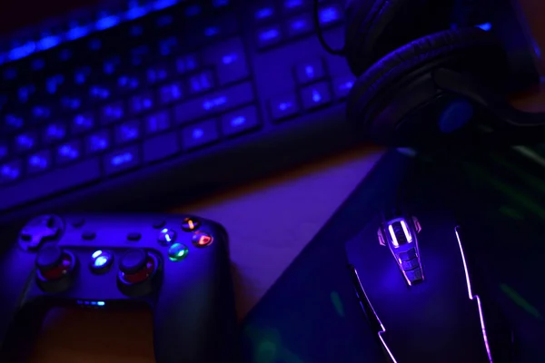 Modern gamepad and gaming mouse lies with keyboard and headphones on table in dark playroom scene. Video game challenges and competitions concept — 스톡 사진