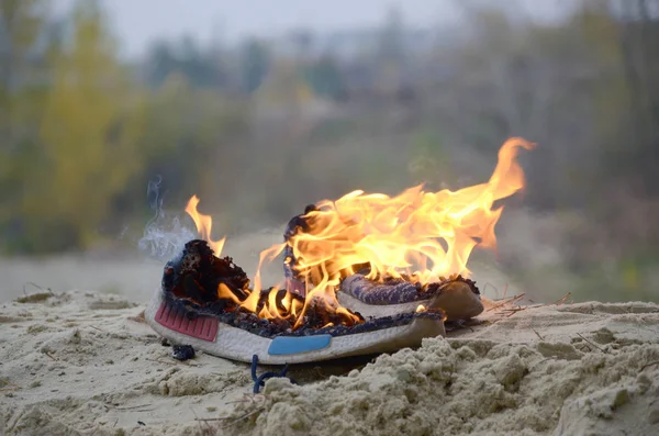 Zapatillas deportivas quemadas o zapatos de gimnasio en el puesto de fuego en la costa de la playa de arena. Atleta agotado. Ejercicio físico durante el concepto de entrenamiento — Foto de Stock