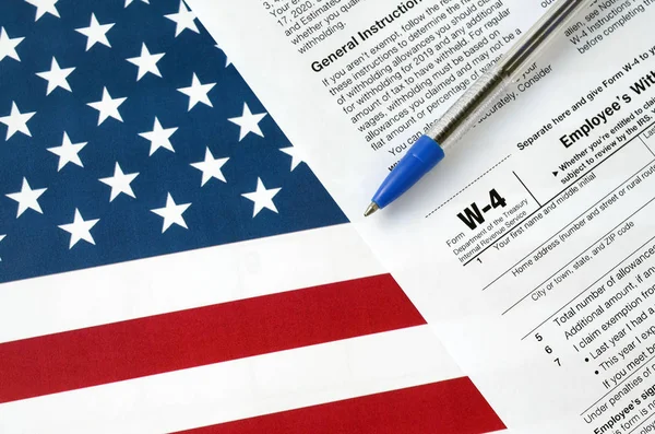 Form W-4 Employee's withholding allowance certificate and blue pen on United States flag. Internal revenue service tax form — 스톡 사진