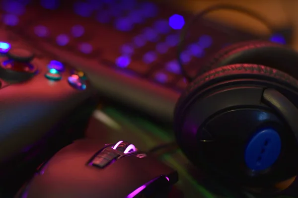 Moderne gamepad en gaming muis ligt met toetsenbord en hoofdtelefoon op tafel in donkere speelkamer scène. Elektronische apparatuur en technologie — Stockfoto