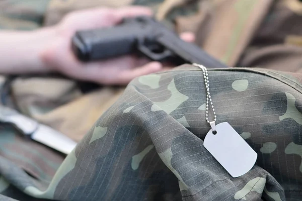 Dog tag with armed hand of dead recruit of Russian army lies on many camouflage clothes