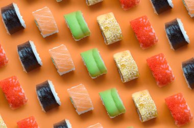 Turuncu arka planda farklı Asya suşi çeşitleri var. Minimalizm üst görünüm düz Japon yemekleri ile yatıyordu