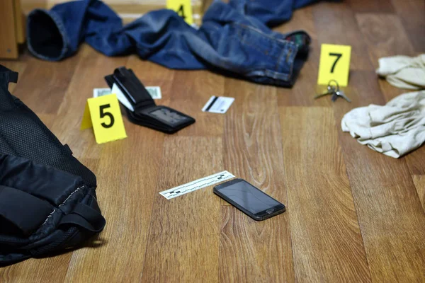 Investigación de la escena del crimen - numeración de las pruebas después del asesinato en el apartamento. Smartphone roto, billetera y ropa con marcadores de evidencia —  Fotos de Stock