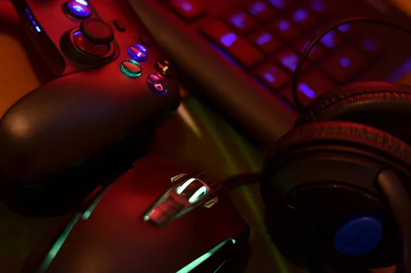 Modernes Gamepad und Gaming-Maus liegt mit Tastatur und Kopfhörer auf dem Tisch in dunklen Spielzimmer Szene. Wettbewerbskonzept für Computerspiele — Stockfoto