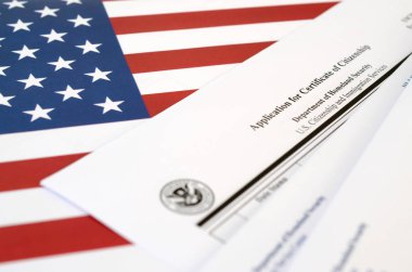 N-600 Application for Certificate of Citizenship blank form lies on United States flag with envelope from Department of Homeland Security clipart