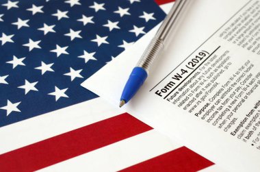 Form W-4 çalışanı harçlık sertifikası talimatlarını ve Birleşik Devletler bayrağında mavi kalemi saklıyor. İç Gelir Vergisi Formu
