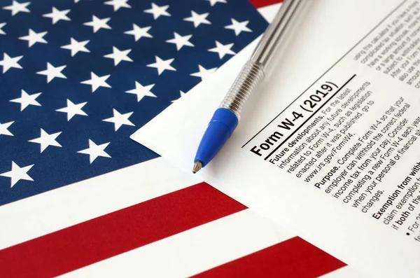 Форма W-4 Сотрудник удерживает пособие сертификат и синяя ручка на флаге США. Налоговая форма службы внутренних доходов — стоковое фото
