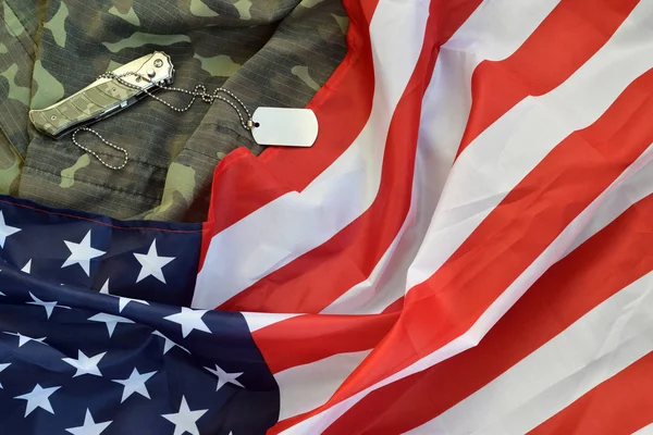 Army dog tag token and knife lies on Old Camouflage uniform and folded United States Flag — Stock Photo, Image