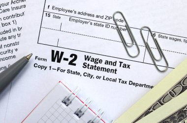 Kalem, defter ve dolar faturaları olduğu vergi formu W-2 üzerinde yatıyor W