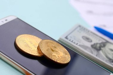 Vergi formları, yüz dolar faturaları ve açık mavi renkli smartphone ile Bitcoins yatıyor. Gelir vergisi beyannamesi