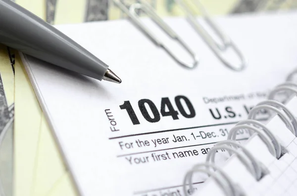 A caneta, caderno e notas de dólar está no formulário de imposto 1040 — Fotografia de Stock