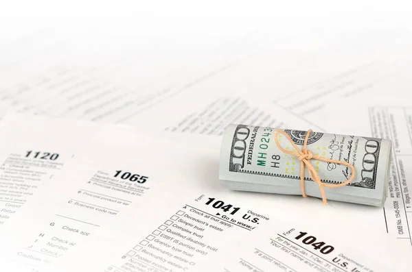 Os formulários fiscais estão perto do rolo de notas de cem dólares. Declaração de imposto sobre o rendimento — Fotografia de Stock