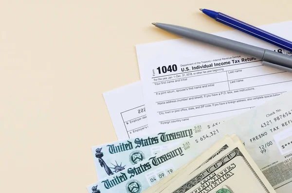 1040 Formulário de declaração de imposto de renda individual com cheque de reembolso e notas de cem dólares em fundo bege — Fotografia de Stock