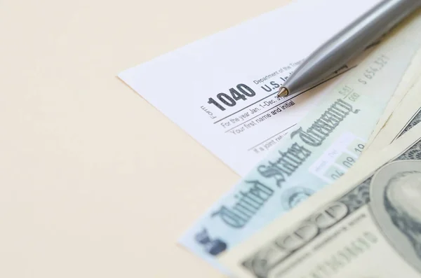 1040 Individual Income tax return form with Refund Check and hundred dollar bills on beige background