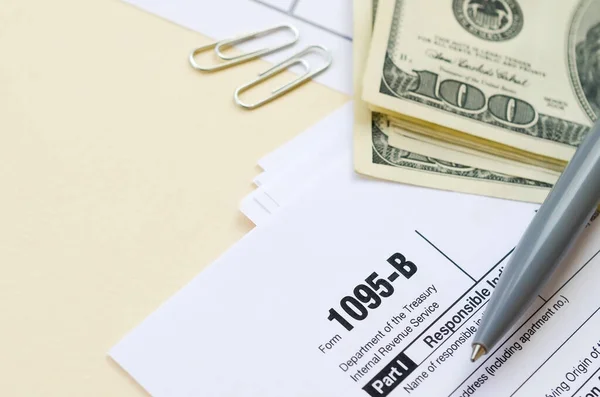 Formulário de IRS 1095-B Saúde Cobertura de imposto em branco está com caneta e muitas centenas de notas de dólar na página de calendário — Fotografia de Stock