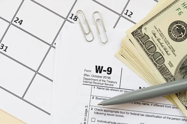 Irs Form W-9納税者識別番号と証明書のブランクはペンであり、カレンダーページには数百ドルの請求書があります。 — ストック写真