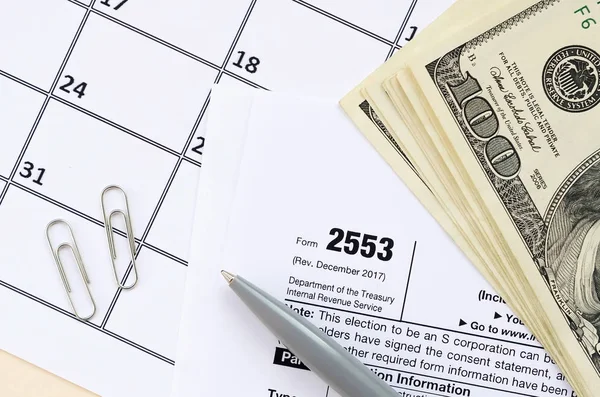 IRS Formulaire 2553 Choix d'une société exploitant une petite entreprise vierge d'impôt se trouve au stylo et plusieurs centaines de billets de dollars sur la page du calendrier — Photo