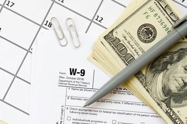 Έντυπο W-9 Αίτημα για τον αριθμό φορολογικού μητρώου των φορολογουμένων και την πιστοποίηση κενό βρίσκεται με στυλό και πολλές εκατοντάδες δολάρια χαρτονομίσματα στην ημερολογιακή σελίδα — Φωτογραφία Αρχείου