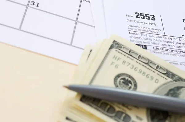 IRS Form 2553 Election by a Small Business Corporation tax blank lies with pen and many hundred dollar bills on calendar page — Stock Photo, Image