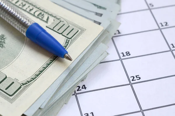 Pen and many hundred US dollar bills on calendar page close up Stock Photo