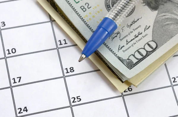 Pen and many hundred US dollar bills on calendar page close up Royalty Free Stock Images