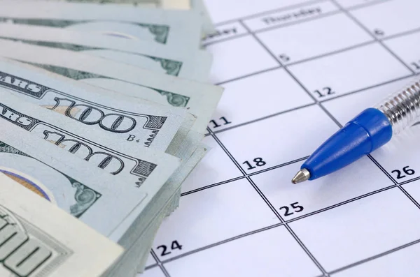 Pen and many hundred US dollar bills on calendar page close up Stock Image