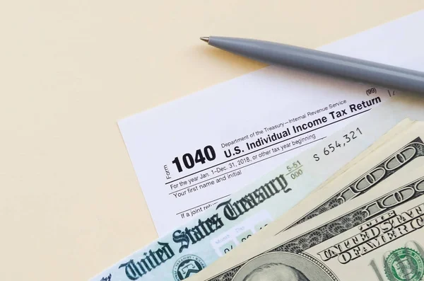 1040 Individual Income tax return form with Refund Check and hundred dollar bills on beige background