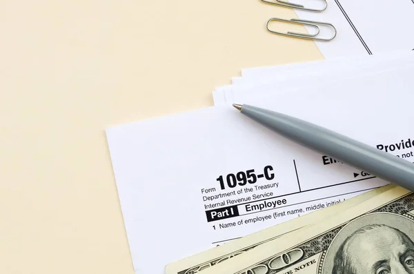 Formulário de IRS 1095-C Oferta de seguro de saúde fornecido pelo empregador e cobertura de impostos em branco está com caneta e muitas centenas de notas de dólar na página de calendário — Fotografia de Stock