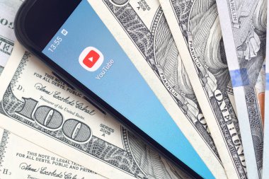 Kharkov, Ukrayna - 6 Şubat 2020: Youtube uygulamalı akıllı telefon ekranı ve bir sürü yüz dolarlık banknotlar. İş ve sosyal ağ kavramı