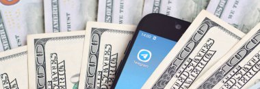 Kharkov, Ukrayna - 6 Şubat 2020: Telgraf uygulamalı akıllı telefon ekranı ve bir sürü yüz dolarlık banknot. İş ve sosyal ağ kavramı