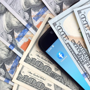 Kharkov, Ukrayna - 6 Şubat 2020: Facebook uygulamalı akıllı telefon ekranı ve bir sürü yüz dolarlık banknot. İş ve sosyal ağ kavramı