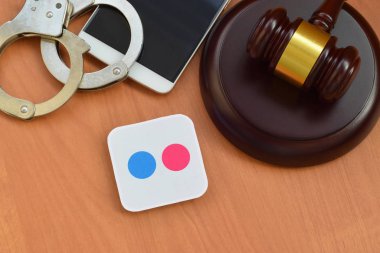 KHARKOV, UKRAINE - FEBRUARY 17, 2020: Flickr paper logo lies with wooden judge gavel, smartphone and handcuffs. Entertainment lawsuit concept