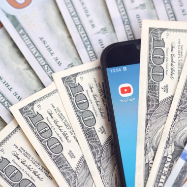 Kharkov, Ukrayna - 6 Şubat 2020: Youtube uygulamalı akıllı telefon ekranı ve bir sürü yüz dolarlık banknotlar. İş ve sosyal ağ kavramı