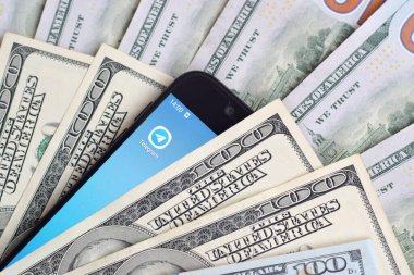 Kharkov, Ukrayna - 6 Şubat 2020: Telgraf uygulamalı akıllı telefon ekranı ve bir sürü yüz dolarlık banknot. İş ve sosyal ağ kavramı