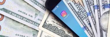 Kharkov, Ukrayna - 6 Şubat 2020: Instagram uygulamalı akıllı telefon ekranı ve bir sürü yüz dolarlık banknot. İş ve sosyal ağ kavramı