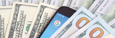 Kharkov, Ukrayna - 6 Şubat 2020: Google uygulamalı akıllı telefon ekranı ve bir sürü yüz dolarlık banknot. İş ve sosyal ağ kavramı