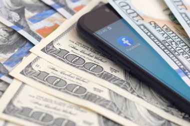 Kharkov, Ukrayna - 6 Şubat 2020: Facebook uygulamalı akıllı telefon ekranı ve bir sürü yüz dolarlık banknot. İş ve sosyal ağ kavramı
