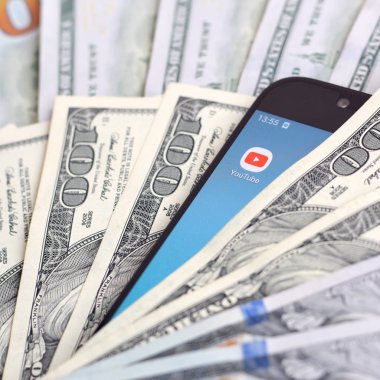Kharkov, Ukrayna - 6 Şubat 2020: Youtube uygulamalı akıllı telefon ekranı ve bir sürü yüz dolarlık banknotlar. İş ve sosyal ağ kavramı