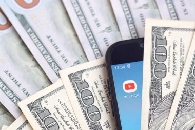 Kharkov, Ukrayna - 6 Şubat 2020: Youtube uygulamalı akıllı telefon ekranı ve bir sürü yüz dolarlık banknotlar. İş ve sosyal ağ kavramı