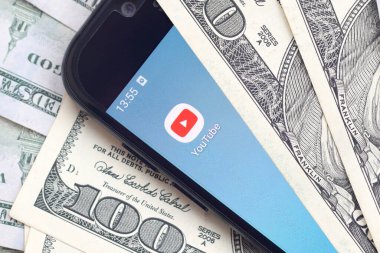 Kharkov, Ukrayna - 6 Şubat 2020: Youtube uygulamalı akıllı telefon ekranı ve bir sürü yüz dolarlık banknotlar. İş ve sosyal ağ kavramı