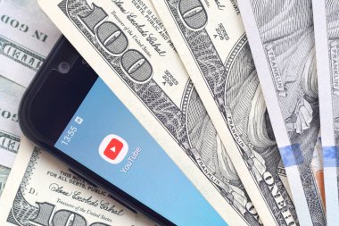 Kharkov, Ukrayna - 6 Şubat 2020: Youtube uygulamalı akıllı telefon ekranı ve bir sürü yüz dolarlık banknotlar. İş ve sosyal ağ kavramı