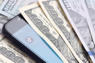 Kharkov, Ukrayna - 6 Şubat 2020: Tiktok uygulamalı akıllı telefon ekranı ve bir sürü yüz dolarlık banknot. İş ve sosyal ağ kavramı