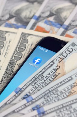 Kharkov, Ukrayna - 6 Şubat 2020: Facebook uygulamalı akıllı telefon ekranı ve bir sürü yüz dolarlık banknot. İş ve sosyal ağ kavramı
